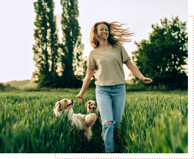 Woman joyfully walking dogs in grassy field.